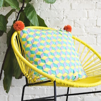 photo d'un coussin avec des pompons aux coins posé sur un fauteuil jaune