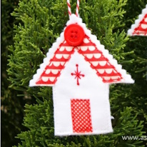 photo d'une décoration en forme de maison rouge et blanche suspendue à un résineux