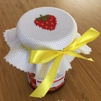 photo d'un pot de confiture couvert d'un carré de canvas ornée d'une fraise au point de croix